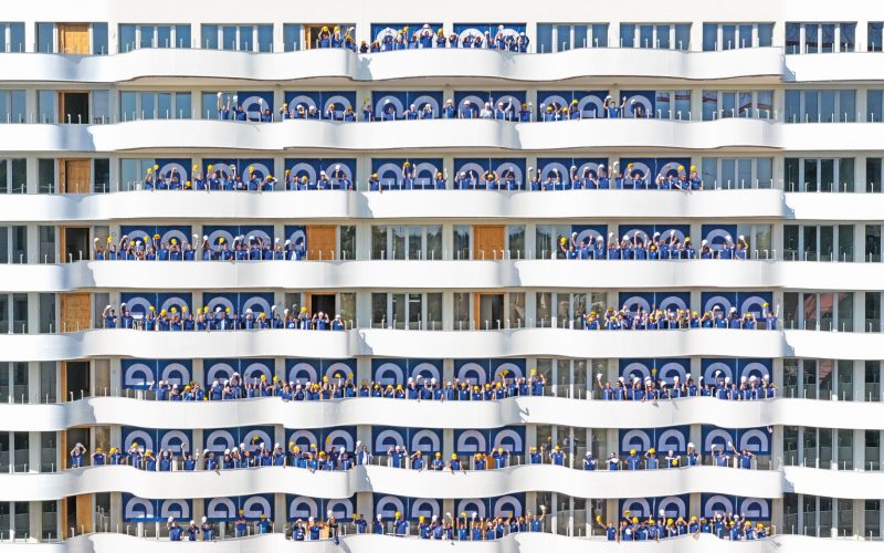 Mitarbeiter der Firma Gemünden bilden das Firmenlogo vor Fenstern eines Mietshauses